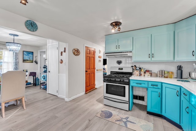 kitchen featuring an inviting chandelier, gas range oven, pendant lighting, decorative backsplash, and light wood-type flooring