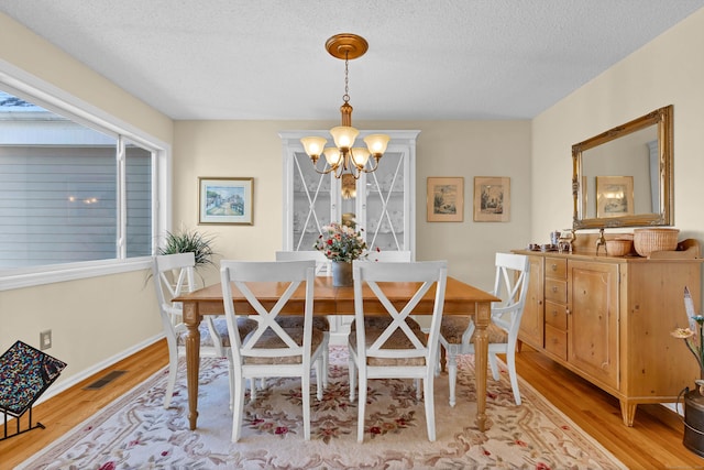 dining area with a textured ceiling, a chandelier, and light hardwood / wood-style flooring