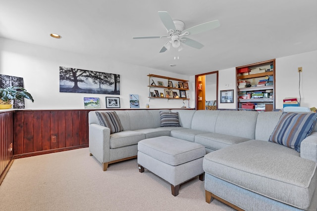 living room featuring ceiling fan, wood walls, and light colored carpet