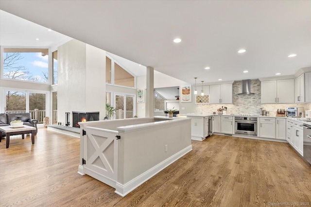 kitchen featuring stainless steel oven, backsplash, wall chimney range hood, decorative light fixtures, and white cabinetry