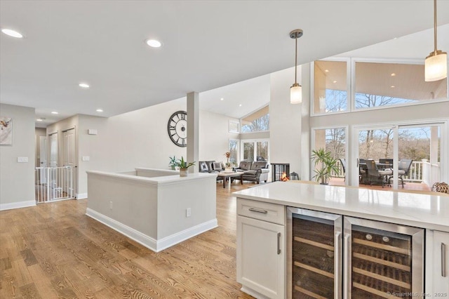 kitchen featuring hanging light fixtures, beverage cooler, light hardwood / wood-style flooring, high vaulted ceiling, and white cabinets