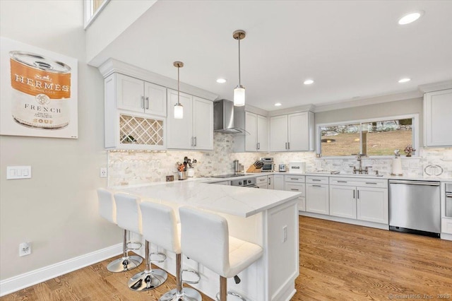 kitchen featuring kitchen peninsula, wall chimney range hood, dishwasher, white cabinetry, and hanging light fixtures