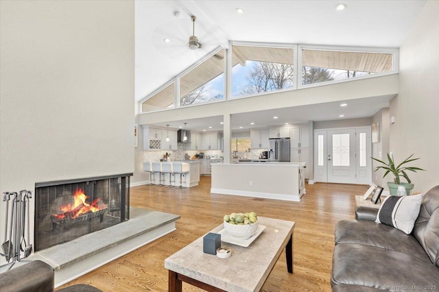 living room with ceiling fan, light hardwood / wood-style flooring, high vaulted ceiling, a multi sided fireplace, and plenty of natural light