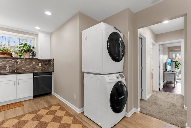 laundry room featuring stacked washer / drying machine, sink, a wealth of natural light, and light hardwood / wood-style flooring