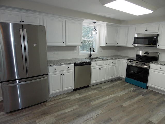 kitchen with white cabinetry, sink, light stone counters, appliances with stainless steel finishes, and light wood-type flooring