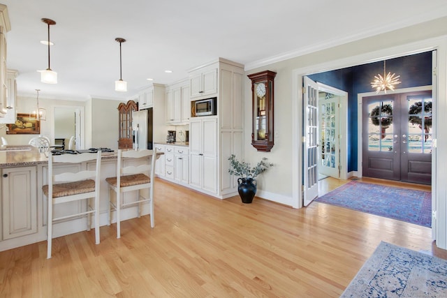 kitchen with french doors, white cabinets, hanging light fixtures, appliances with stainless steel finishes, and a breakfast bar area