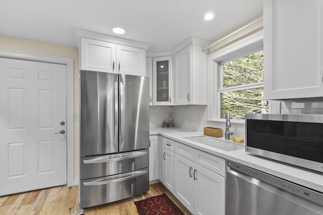 kitchen with sink, light wood-type flooring, appliances with stainless steel finishes, tasteful backsplash, and white cabinetry