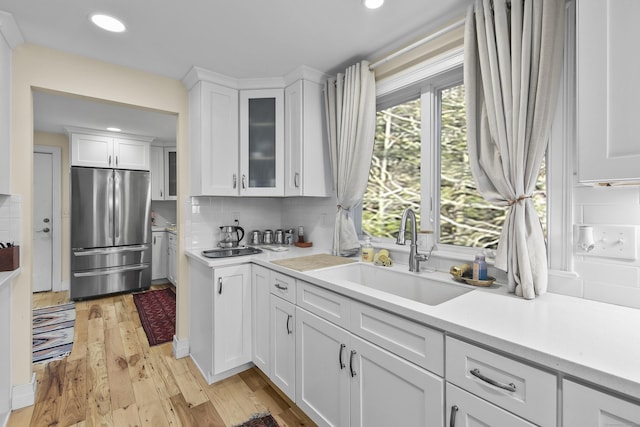 kitchen featuring stainless steel refrigerator, sink, tasteful backsplash, light hardwood / wood-style floors, and white cabinets