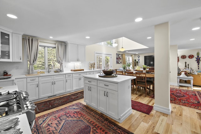 kitchen with range, sink, decorative backsplash, light wood-type flooring, and white cabinetry