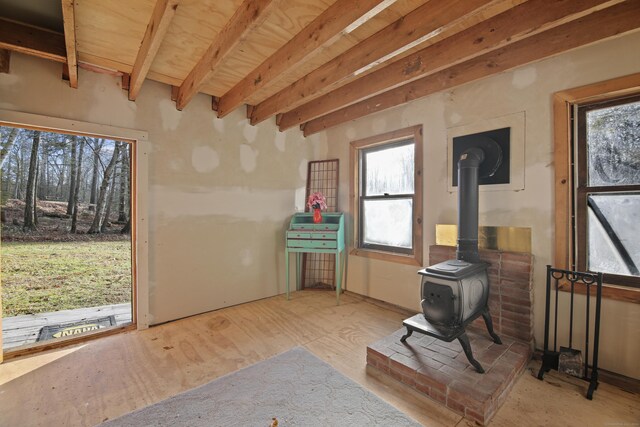 miscellaneous room featuring beam ceiling, a wood stove, and a healthy amount of sunlight