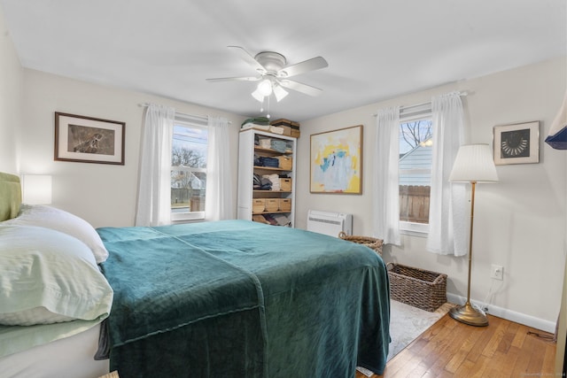 bedroom featuring an AC wall unit, multiple windows, ceiling fan, and hardwood / wood-style floors