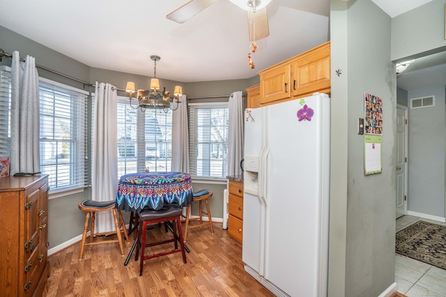 kitchen featuring pendant lighting, ceiling fan with notable chandelier, light wood-type flooring, white fridge with ice dispenser, and light brown cabinetry