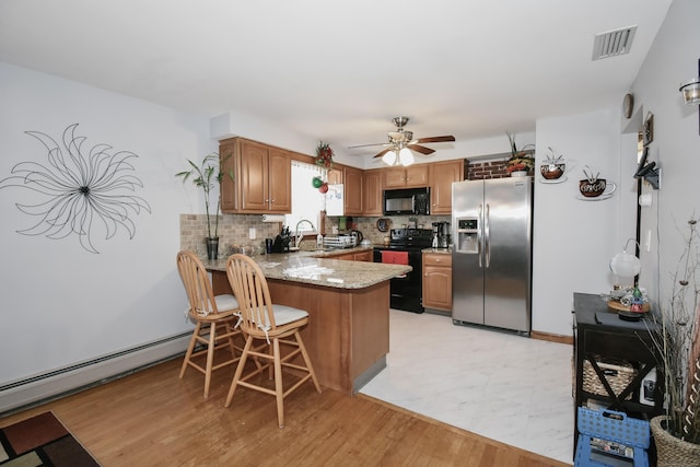 kitchen with ceiling fan, a baseboard radiator, kitchen peninsula, stone countertops, and black appliances