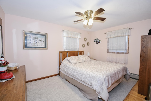 bedroom with light wood-type flooring, ceiling fan, and a baseboard heating unit