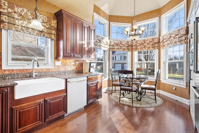 kitchen featuring white dishwasher, a healthy amount of sunlight, sink, pendant lighting, and a chandelier