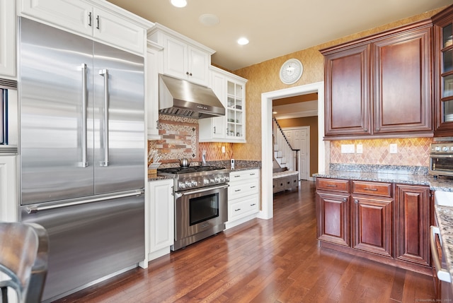 kitchen featuring decorative backsplash, ventilation hood, high end appliances, and dark stone countertops