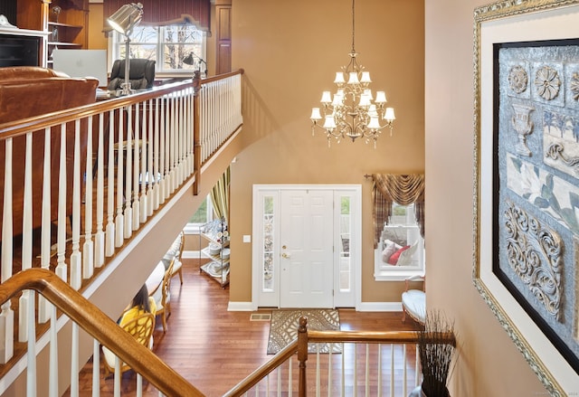 entryway with a towering ceiling, wood-type flooring, and a notable chandelier