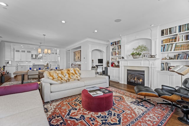 living room with recessed lighting, a notable chandelier, dark wood-style flooring, ornamental molding, and a glass covered fireplace