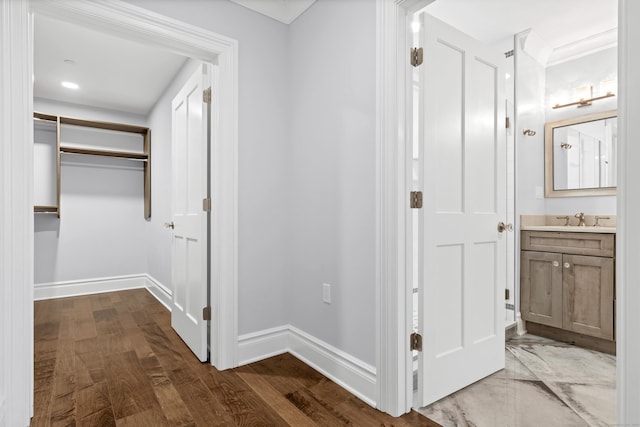 hall featuring a sink, baseboards, and dark wood-style flooring