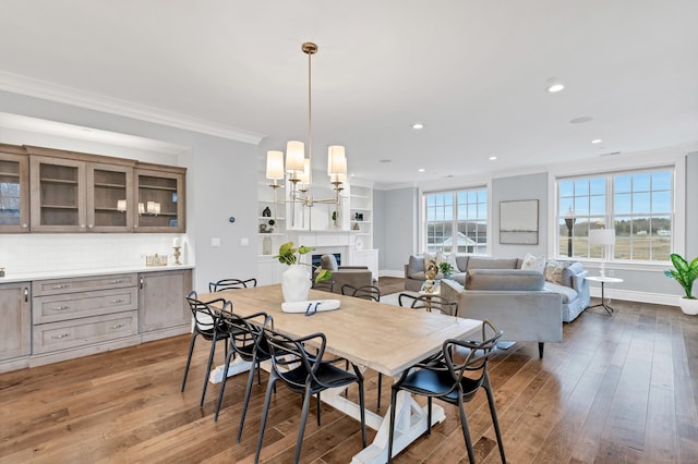 dining room with recessed lighting, a fireplace, ornamental molding, and wood finished floors