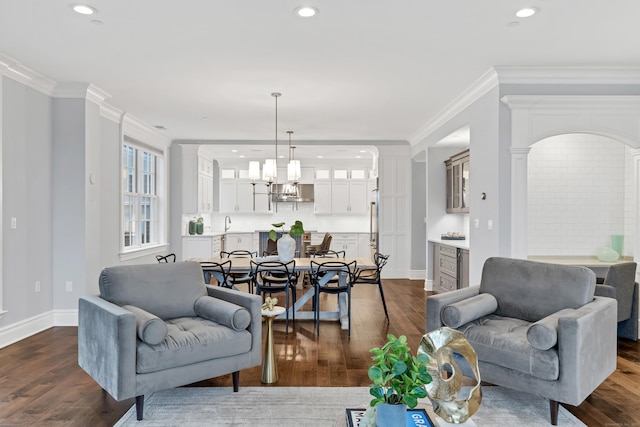 living area with dark wood-style flooring, ornamental molding, and an inviting chandelier