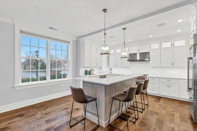 kitchen featuring visible vents, baseboards, a kitchen breakfast bar, under cabinet range hood, and crown molding
