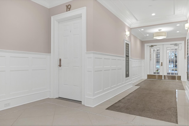 corridor featuring crown molding, light tile patterned floors, a decorative wall, and wainscoting