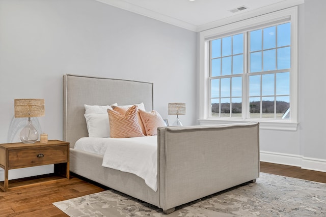 bedroom featuring wood finished floors, baseboards, ornamental molding, and visible vents