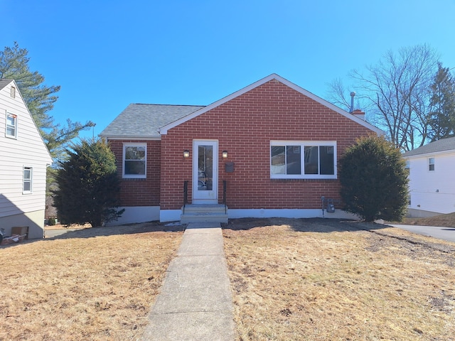 bungalow with roof with shingles, a front lawn, and brick siding