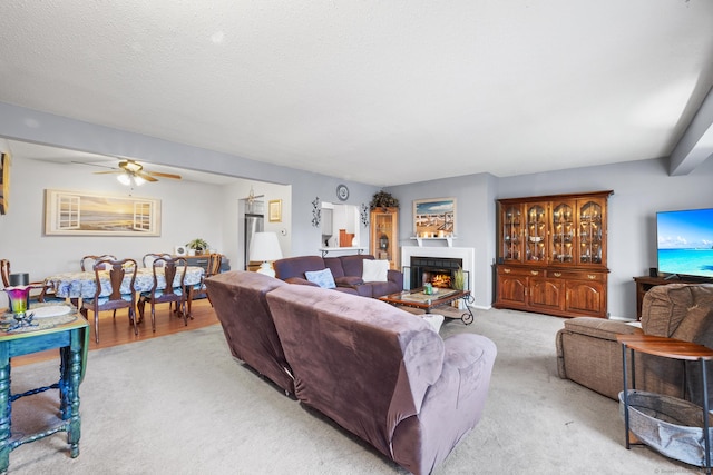 carpeted living room featuring a textured ceiling, ceiling fan, and a tiled fireplace