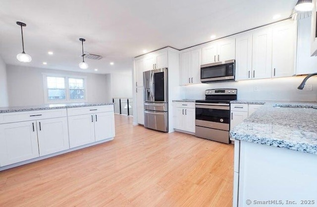 kitchen featuring appliances with stainless steel finishes, sink, light wood-type flooring, white cabinets, and hanging light fixtures