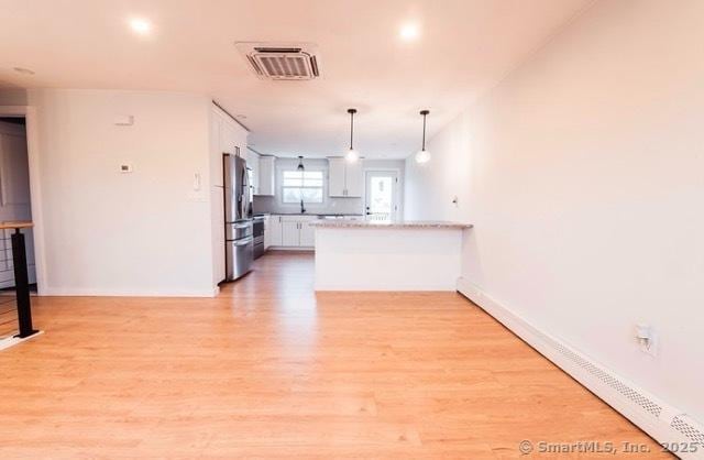 kitchen with stainless steel refrigerator, hanging light fixtures, white cabinetry, and light hardwood / wood-style floors