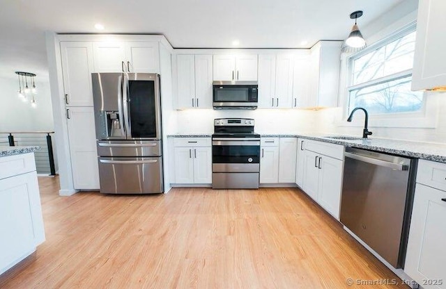 kitchen featuring appliances with stainless steel finishes, decorative light fixtures, light hardwood / wood-style floors, sink, and white cabinetry