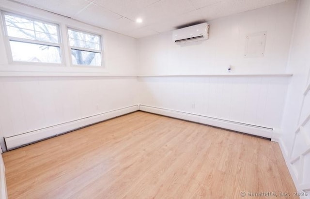 empty room with a wall mounted AC, a paneled ceiling, and light wood-type flooring