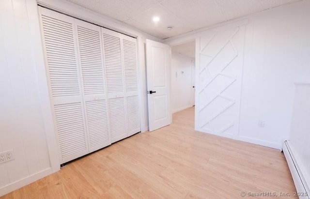 unfurnished bedroom featuring light hardwood / wood-style floors, a paneled ceiling, a baseboard radiator, and a closet