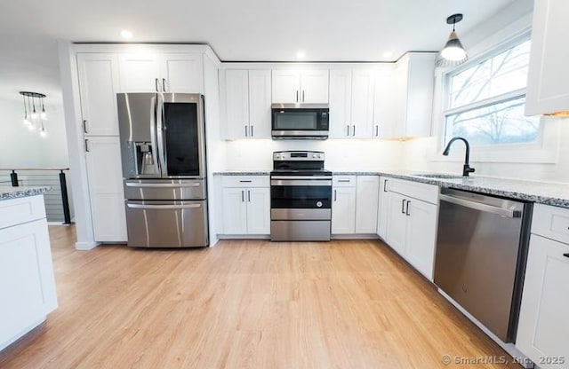 kitchen featuring appliances with stainless steel finishes, sink, white cabinets, hanging light fixtures, and light stone countertops