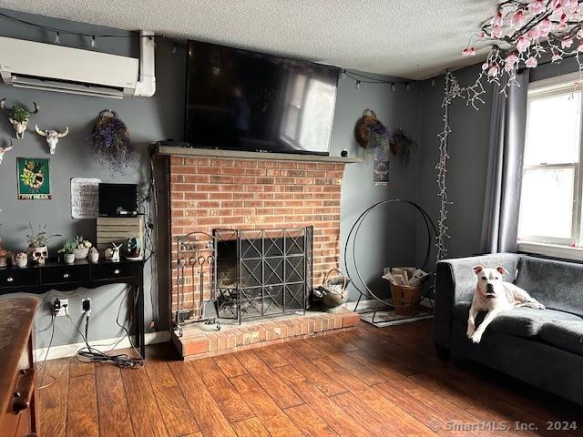 living room featuring hardwood / wood-style flooring, a fireplace, an AC wall unit, and a textured ceiling