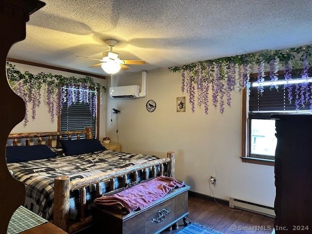 bedroom with a wall mounted air conditioner, dark wood-type flooring, a baseboard heating unit, ceiling fan, and a textured ceiling