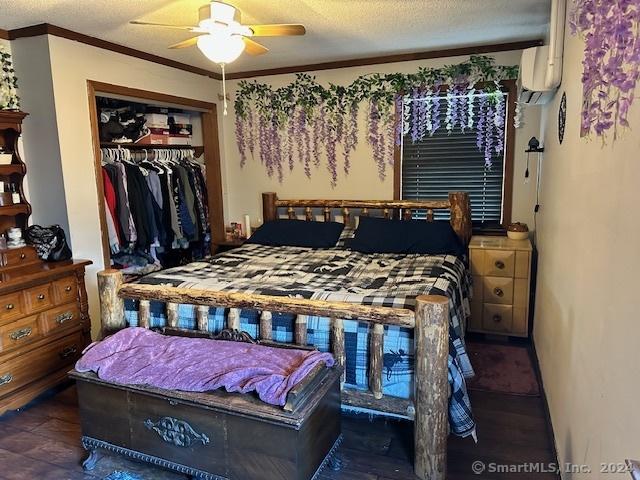 bedroom with ceiling fan, ornamental molding, a textured ceiling, a wall unit AC, and a closet