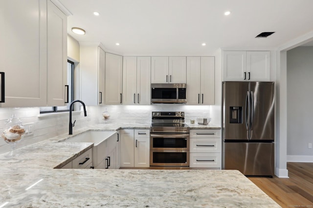 kitchen featuring white cabinetry, appliances with stainless steel finishes, sink, and light stone counters