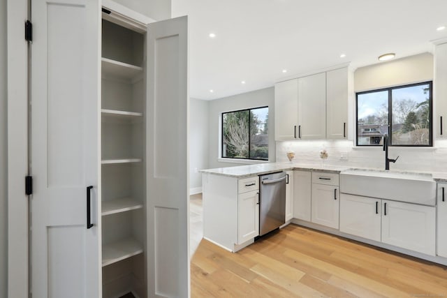 kitchen with sink, light hardwood / wood-style flooring, white cabinetry, light stone countertops, and stainless steel dishwasher