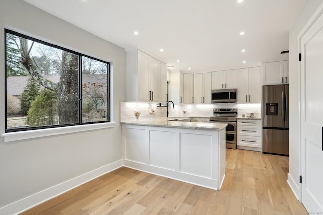 kitchen featuring sink, light hardwood / wood-style flooring, appliances with stainless steel finishes, white cabinetry, and kitchen peninsula