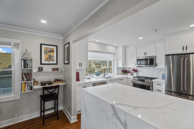 kitchen with crown molding, high quality appliances, light stone counters, white cabinetry, and a sink