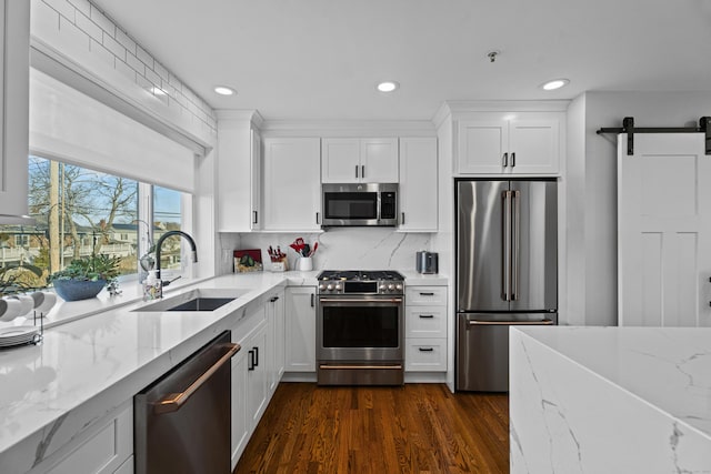 kitchen featuring sink, a barn door, appliances with stainless steel finishes, light stone counters, and white cabinetry