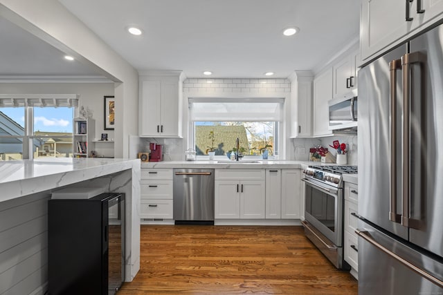 kitchen with dark wood finished floors, a sink, decorative backsplash, stainless steel appliances, and white cabinets