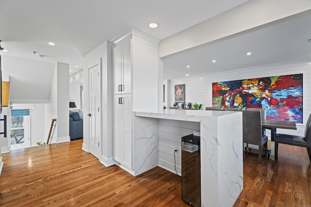 kitchen featuring wood finished floors, light stone countertops, a peninsula, recessed lighting, and white cabinets