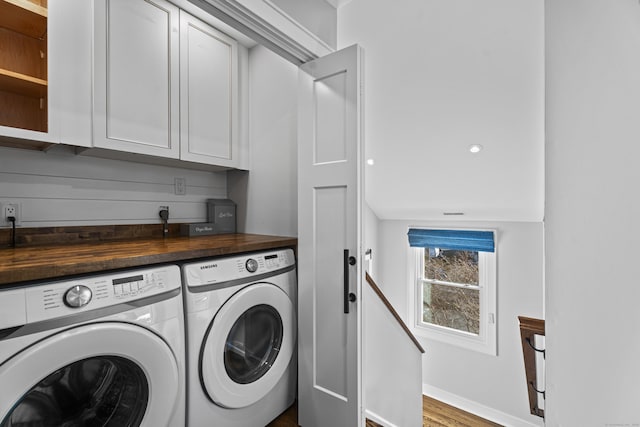 clothes washing area with washing machine and dryer, dark hardwood / wood-style flooring, and cabinets