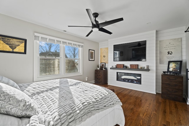 bedroom featuring a fireplace, dark hardwood / wood-style floors, and ceiling fan