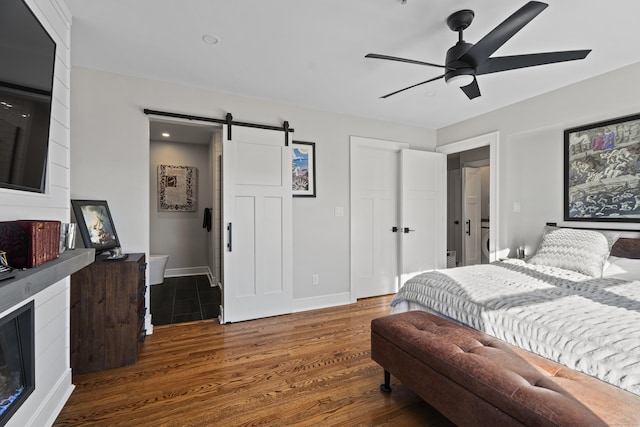 bedroom with wood finished floors, baseboards, a fireplace, ceiling fan, and a barn door