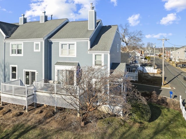 back of property featuring roof with shingles, a deck, and a chimney